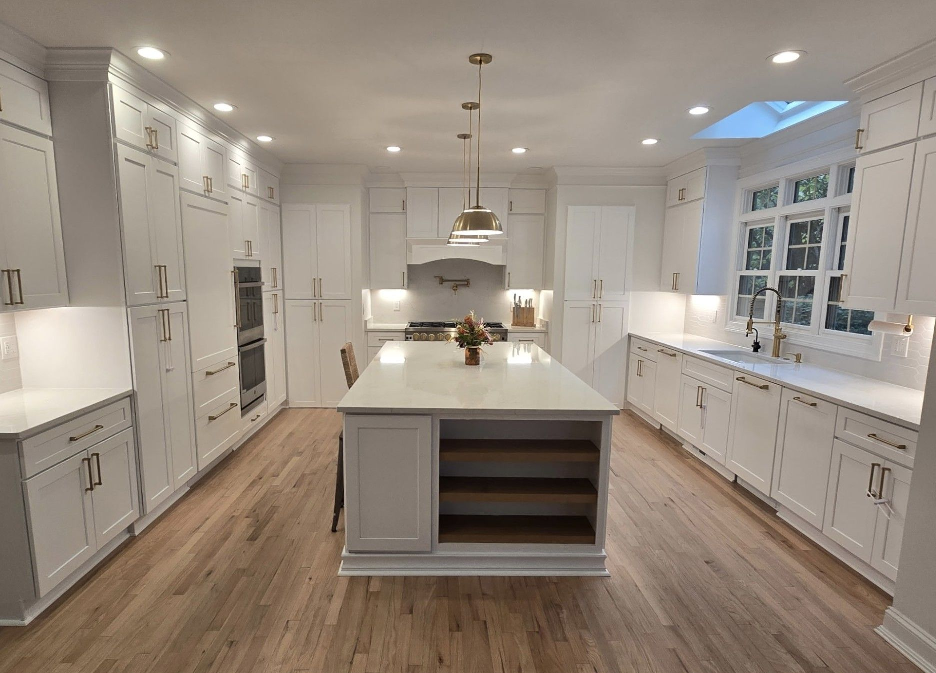 White kitchen with island, cabinets, and appliances on hardwood floors; overhead lighting.