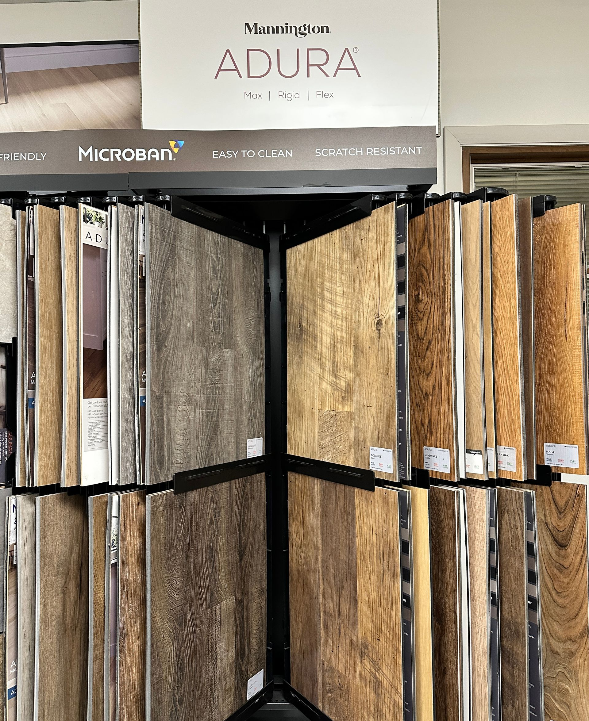 Display of ADURA luxury vinyl plank flooring samples in a showroom, various wood grain colors.