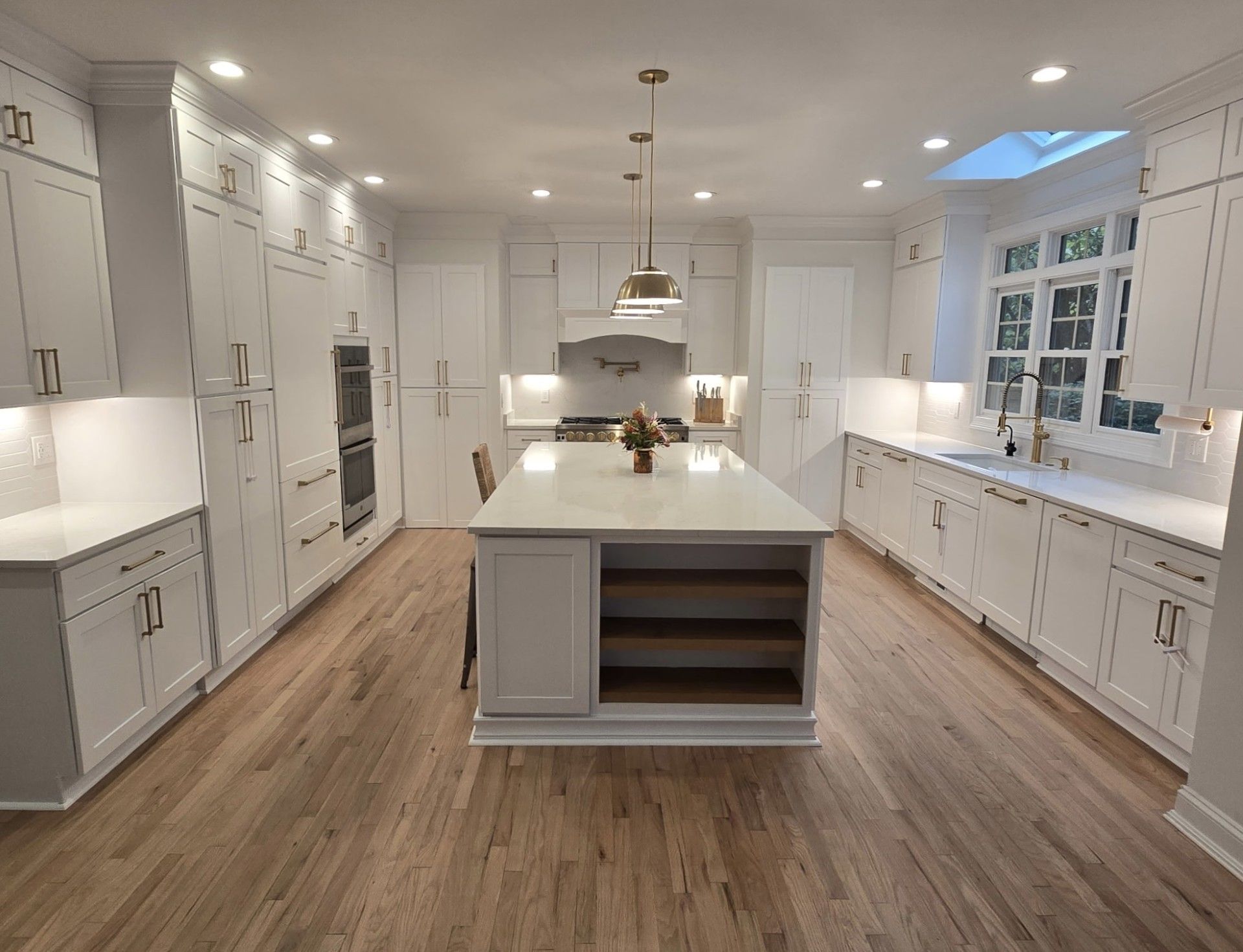 Bright white kitchen with a large island, white cabinets, light wood floor, and a skylight.