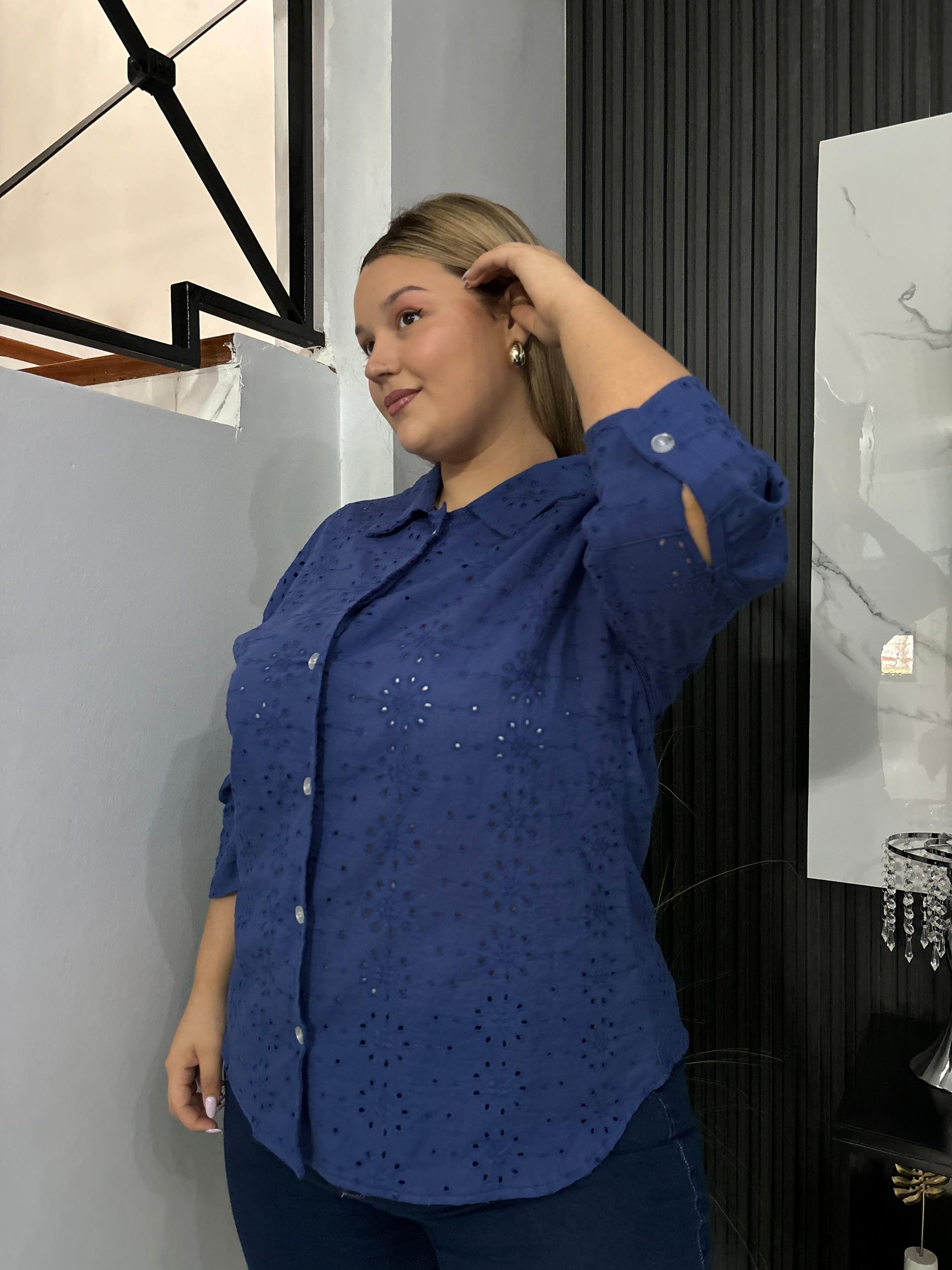 Una mujer con una camisa azul está parada frente a una ventana.