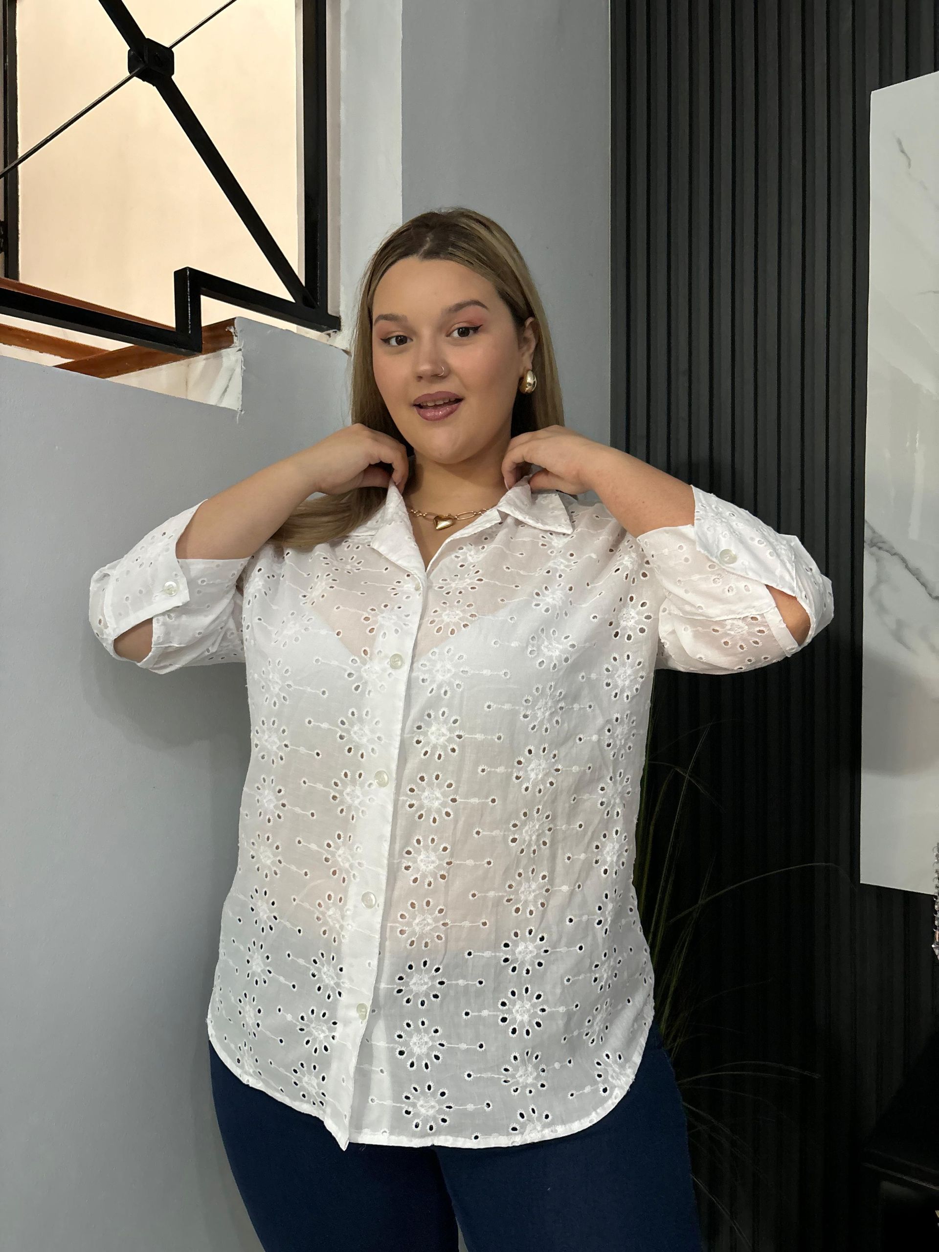 Una mujer con una camisa azul está parada frente a una ventana.