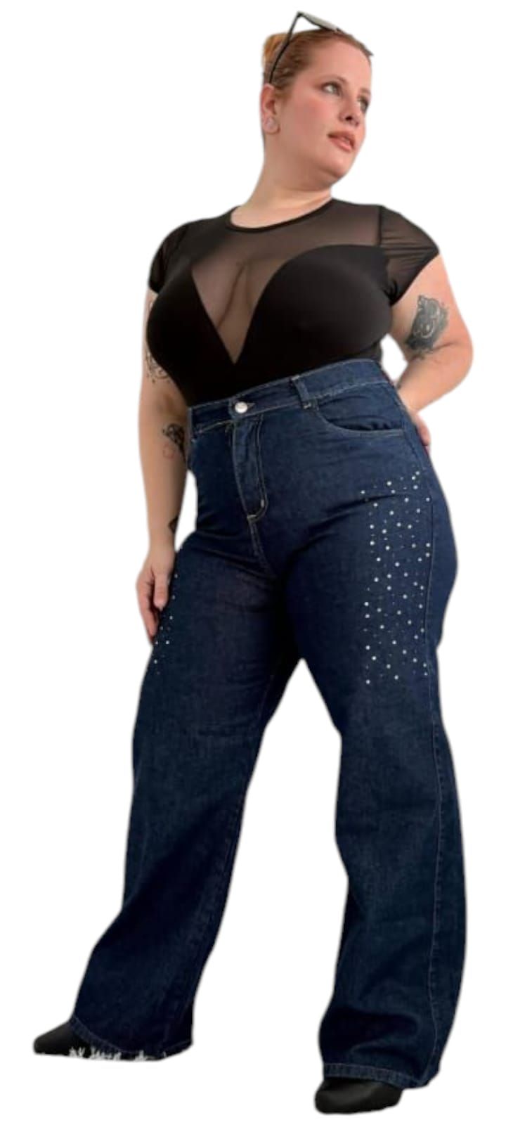 Una mujer con un top negro y jeans anchos está parada sobre un fondo blanco.