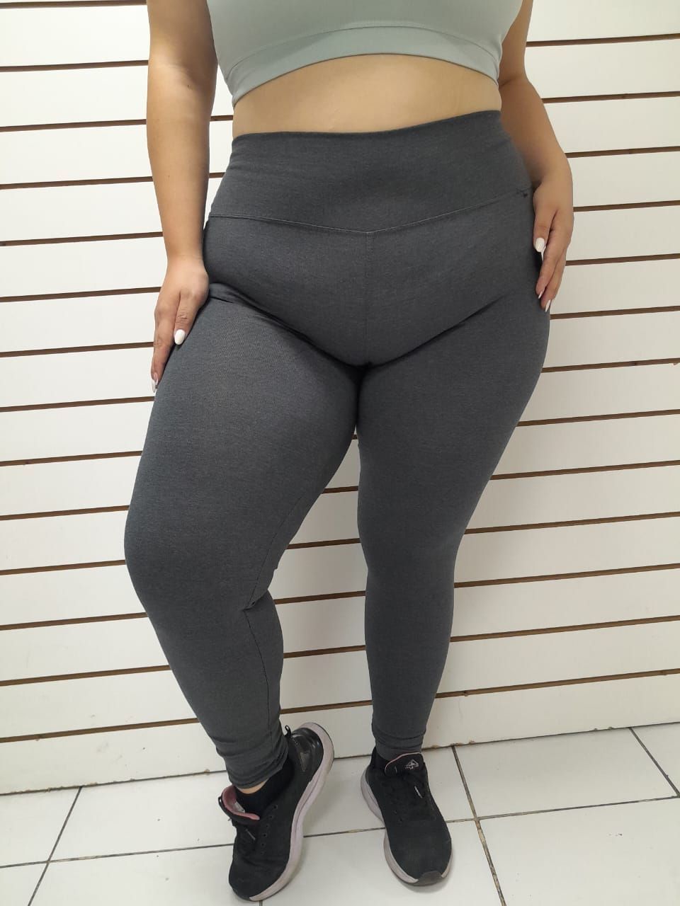 Mujer en sujetador deportivo y mallas, en cuclillas, mirando hacia abajo, en el interior.