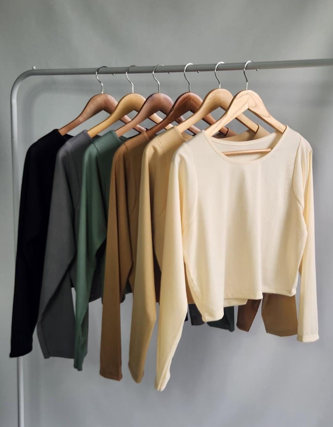 Variedad de tops de manga larga colgados en un perchero, en colores como blanco, beige y verde.