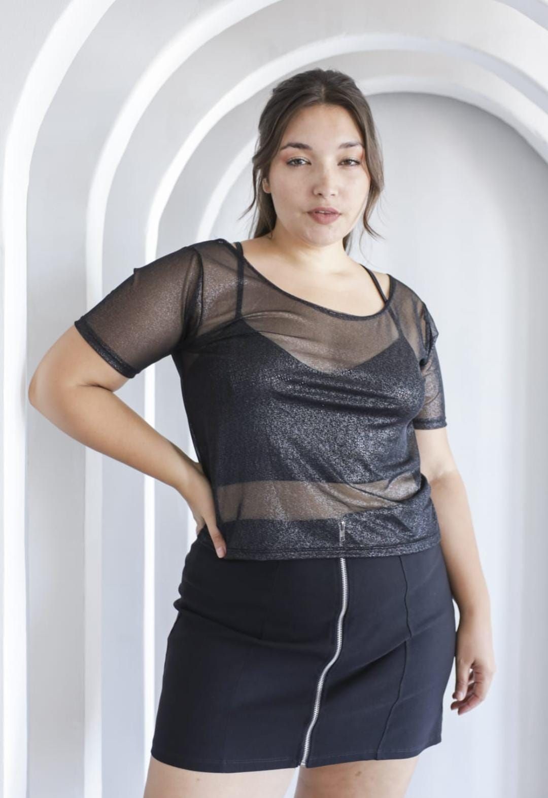 Tres tops cortos negros transparentes y brillantes en perchas de madera, colgados en un estante plateado.