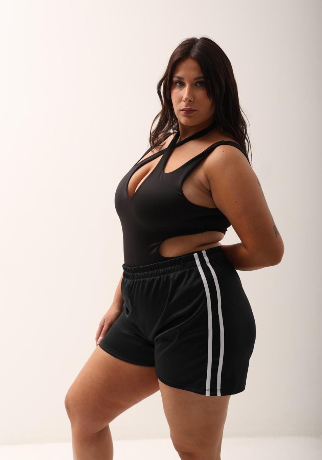 Mujer con traje negro recortado y pantalones cortos negros.