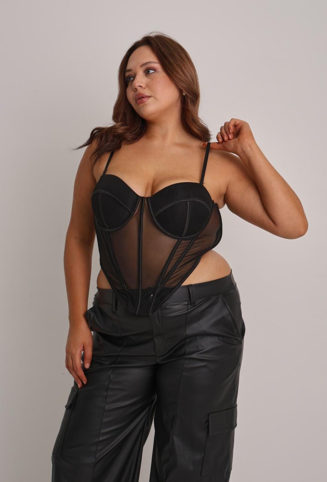 Mujer con corsé negro y pantalones de cuero sintético, posando sobre un fondo blanco.