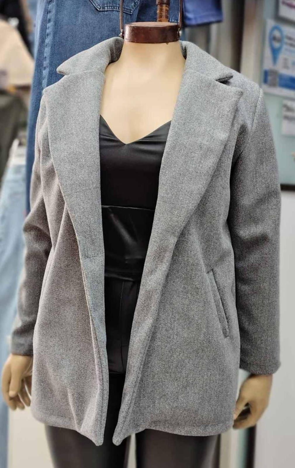 Abrigo verde azulado sobre un maniquí, encima de un top y pantalones negros.