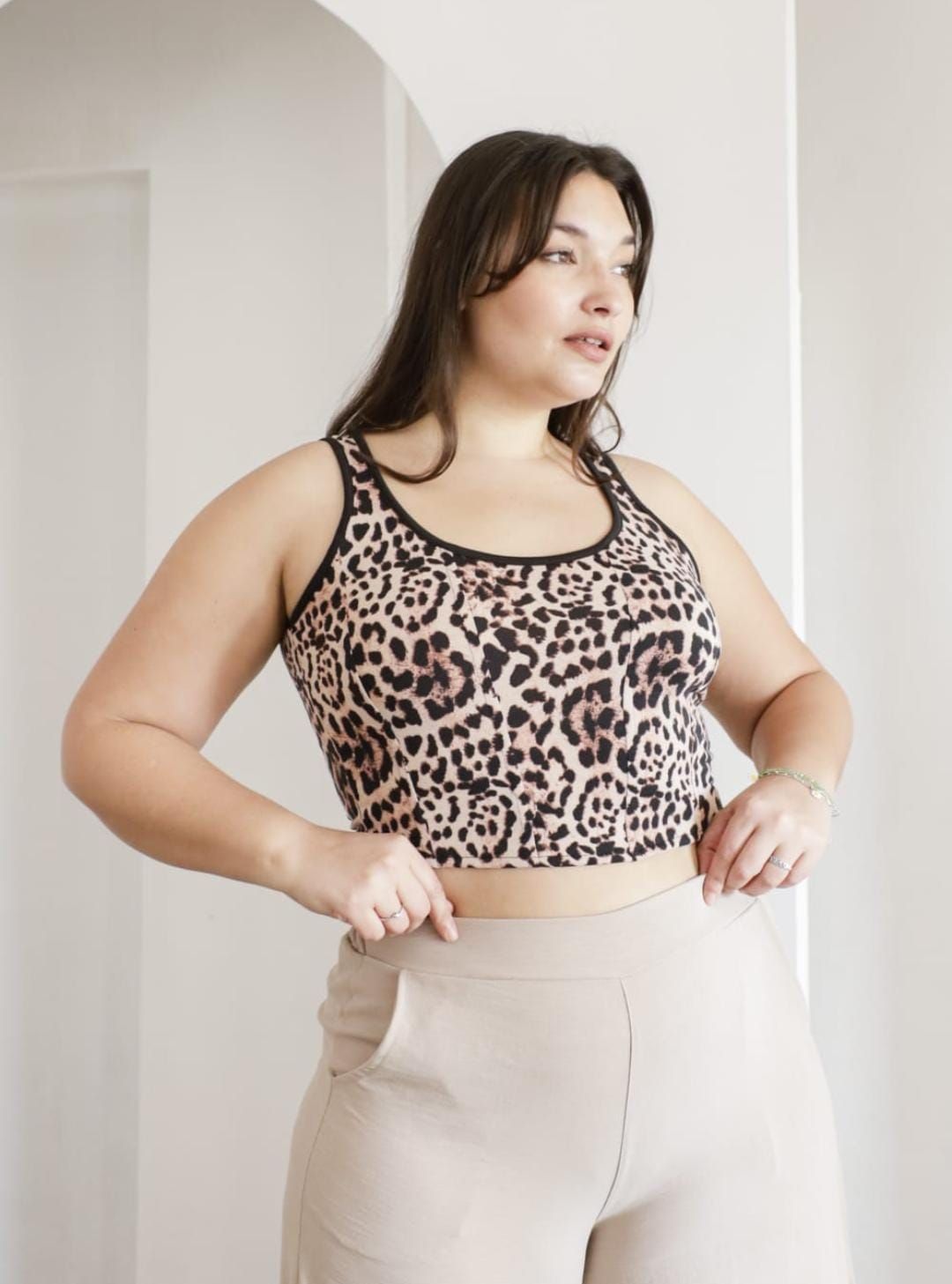 Mujer con top corto con estampado de leopardo y pantalones beige, en el interior.