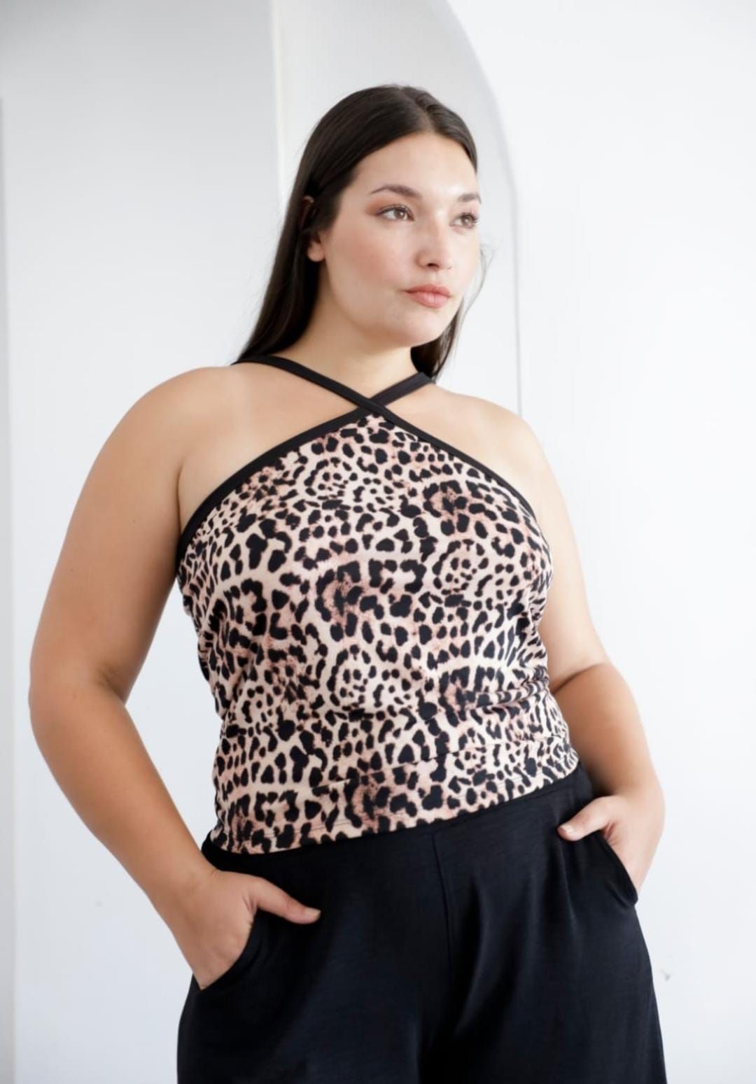 Mujer con top con estampado de leopardo y pantalones negros, mano en el bolsillo, de pie en el interior.