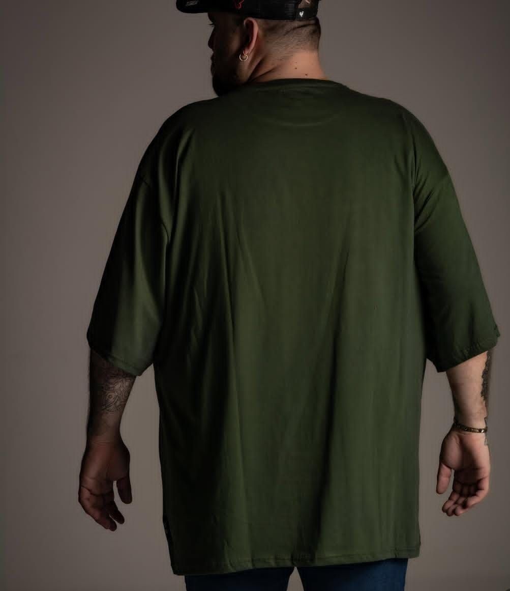 Hombre con barba y tatuajes, con camiseta y gorra verdes con el dibujo de un edificio. Fondo gris.