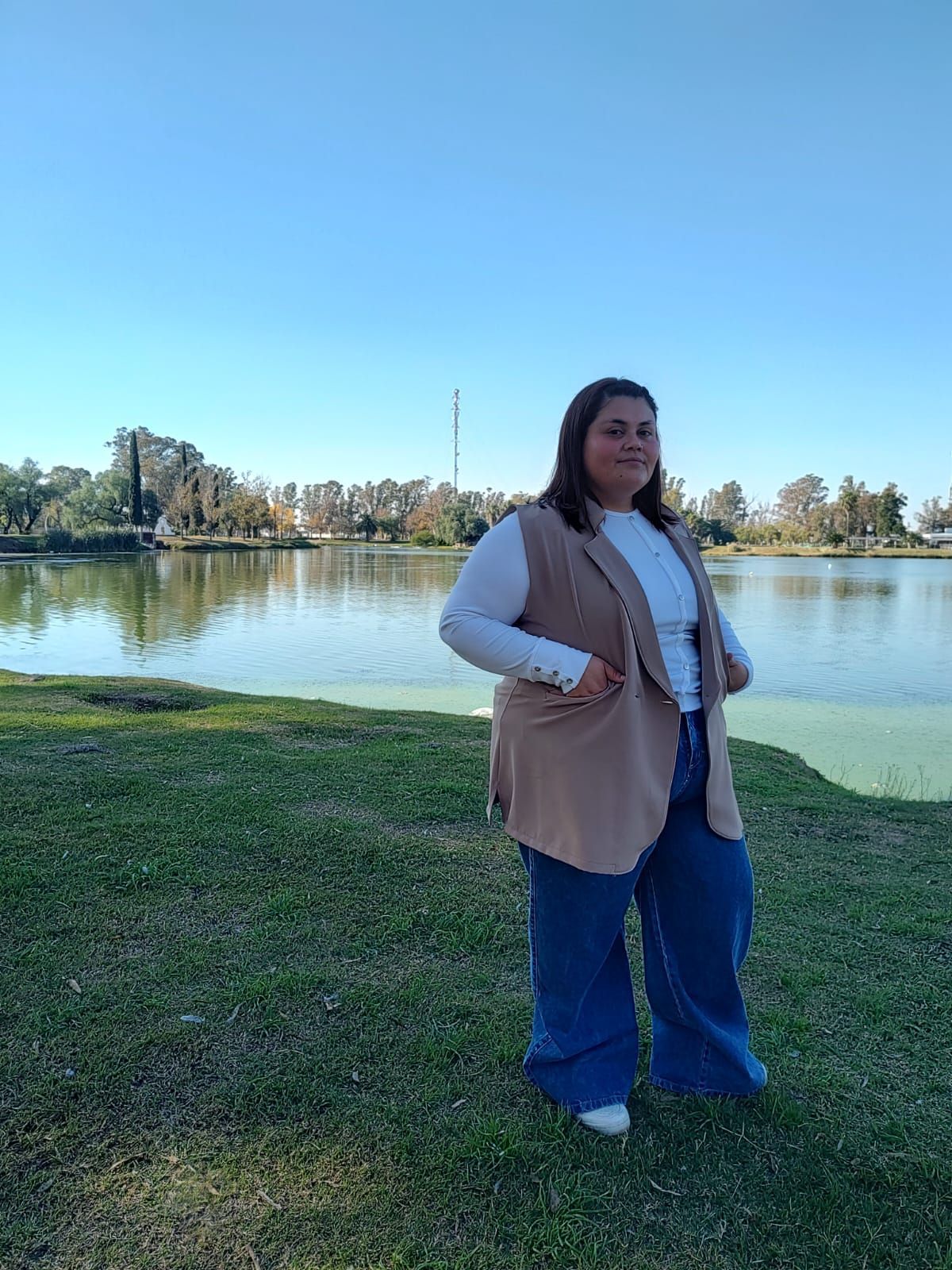 Mujer sonriendo en un parque, vestida con un chaleco color canela
