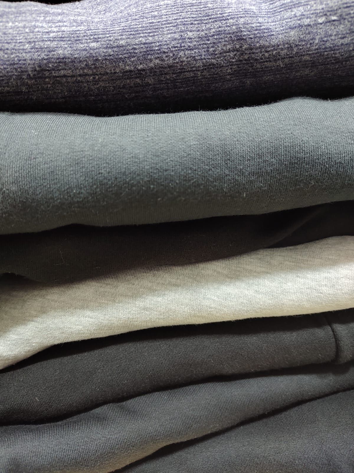 Un hombre con camisa azul claro y pantalones oscuros sonríe al aire libre, con las manos en los bolsillos.