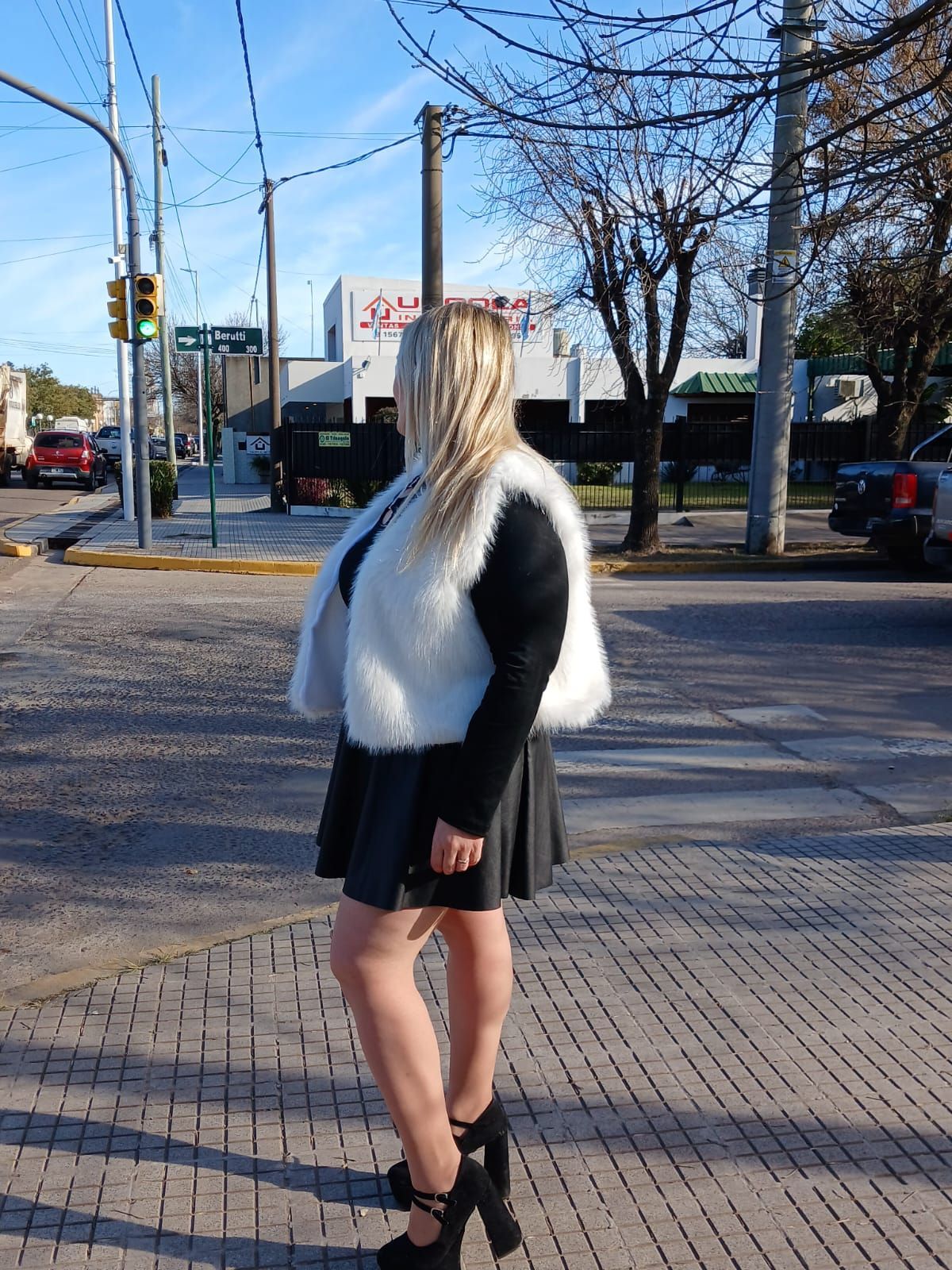 Mujer con chaleco de piel, falda y botas posa en una acera.