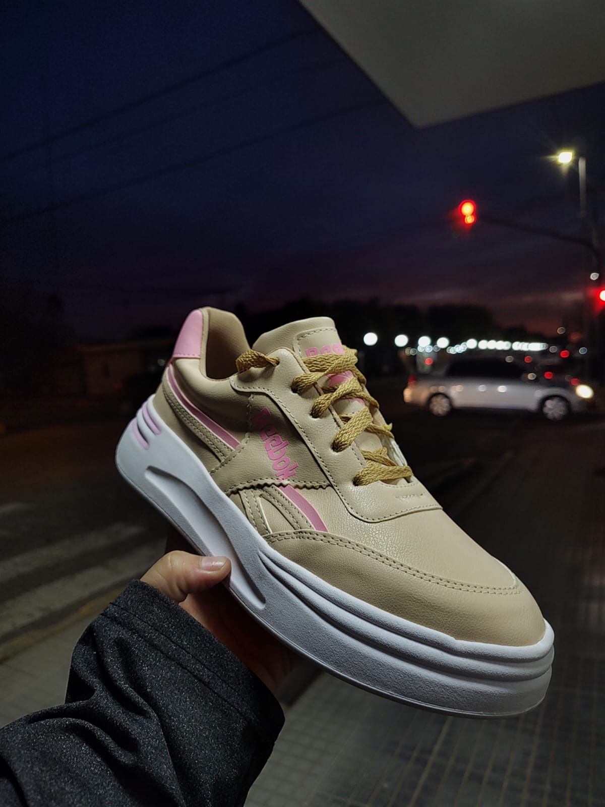 Zapatilla Reebok negra con suela blanca, sostenida en la mano, al aire libre por la noche.