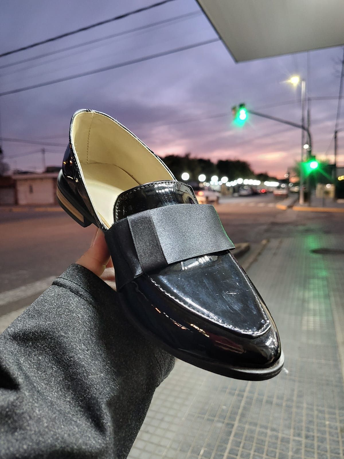 Mocasín con estampado de leopardo y lazo negro sostenido frente a una calle al anochecer.