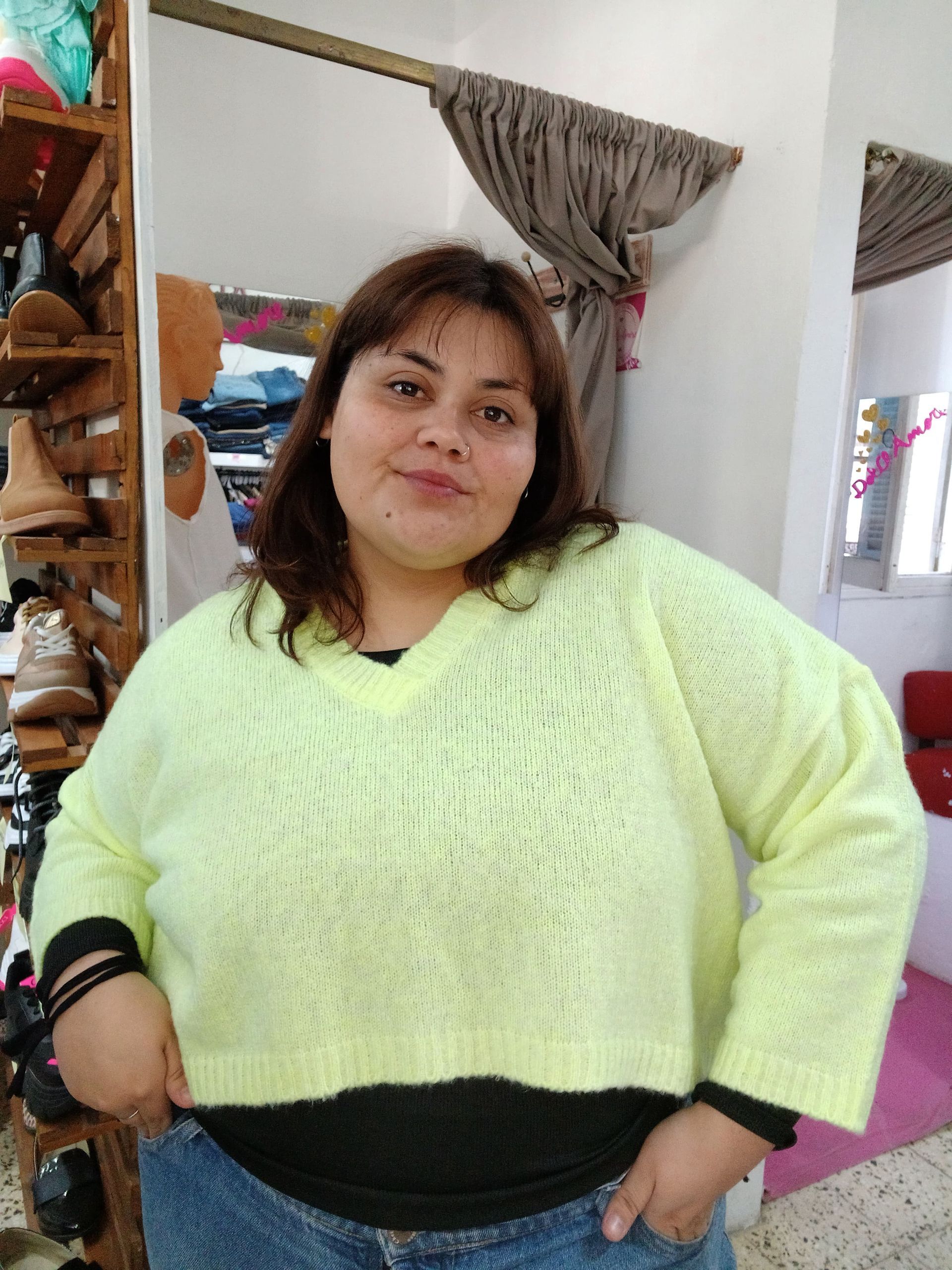 Mujer con suéter de rayas rosas y amarillas, de pie en el interior.