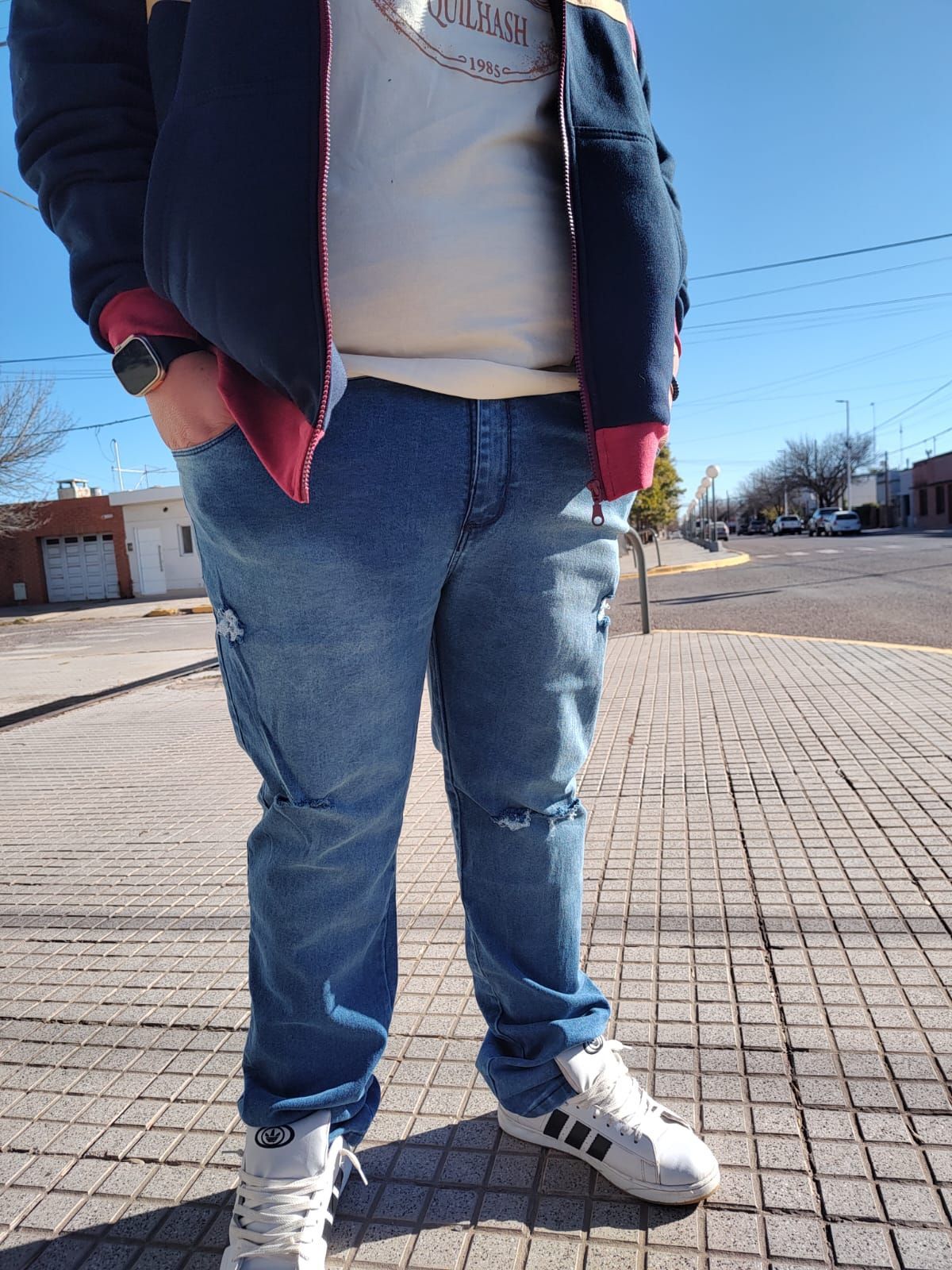 Persona con jeans azules, una chaqueta azul marino con detalles rojos y zapatillas blancas.