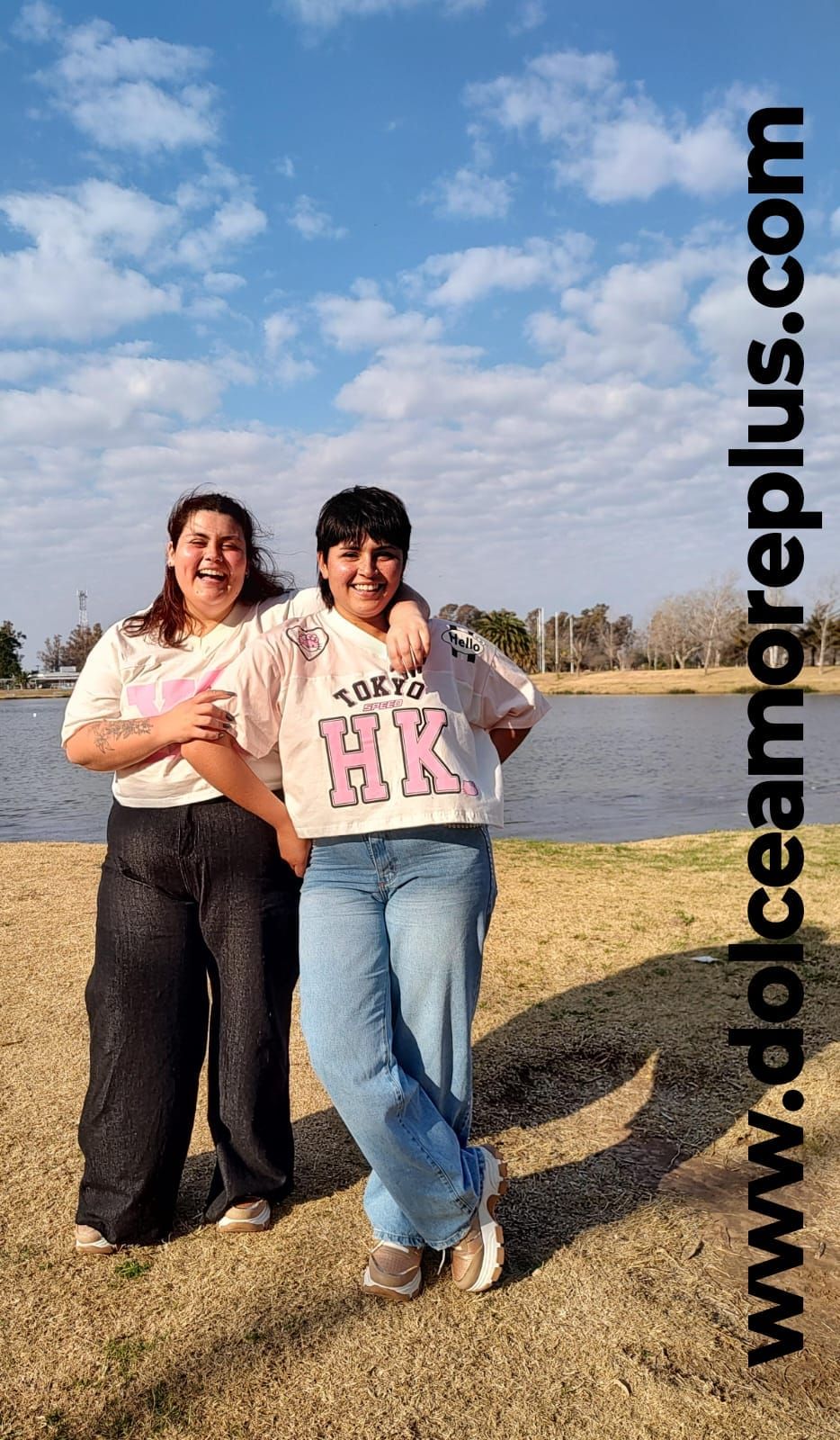 Dos personas están de pie junto a un lago, abrazadas, sonriendo.