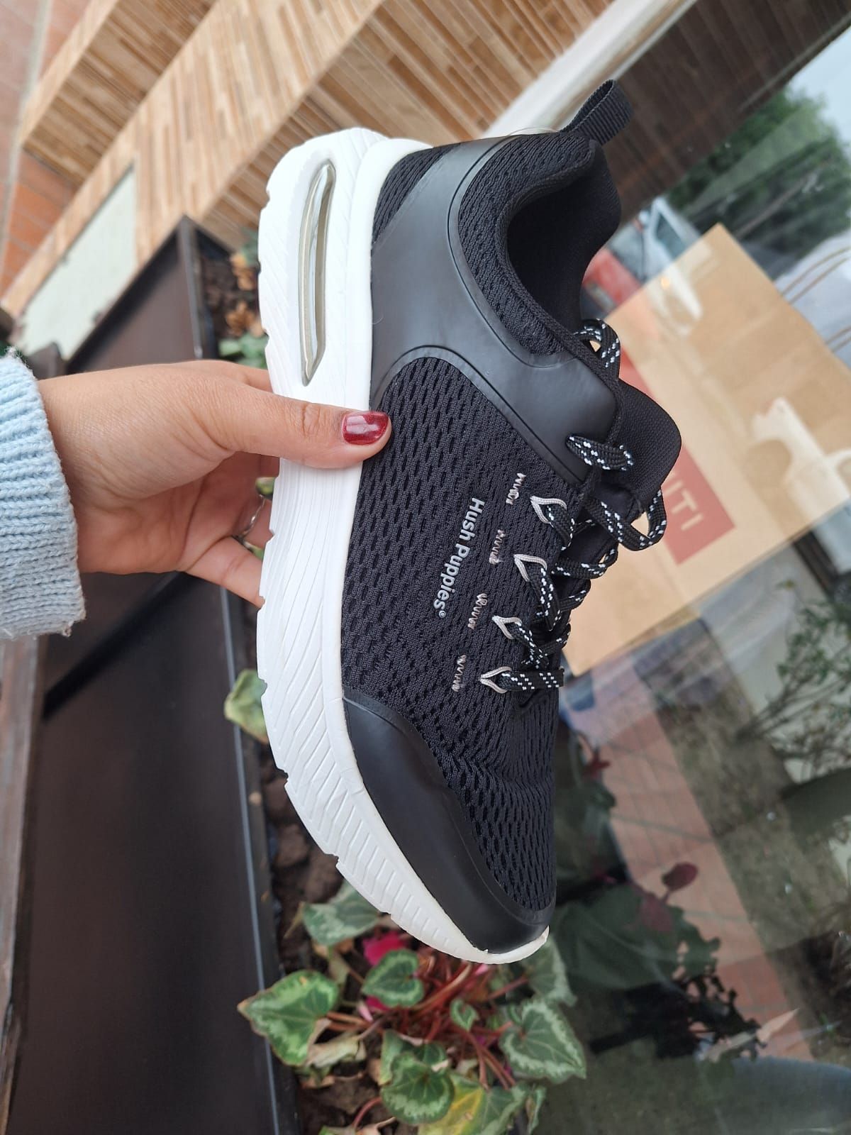 Zapatilla Hush Puppies de color negro con suela blanca y cordones sujetos con una mano.