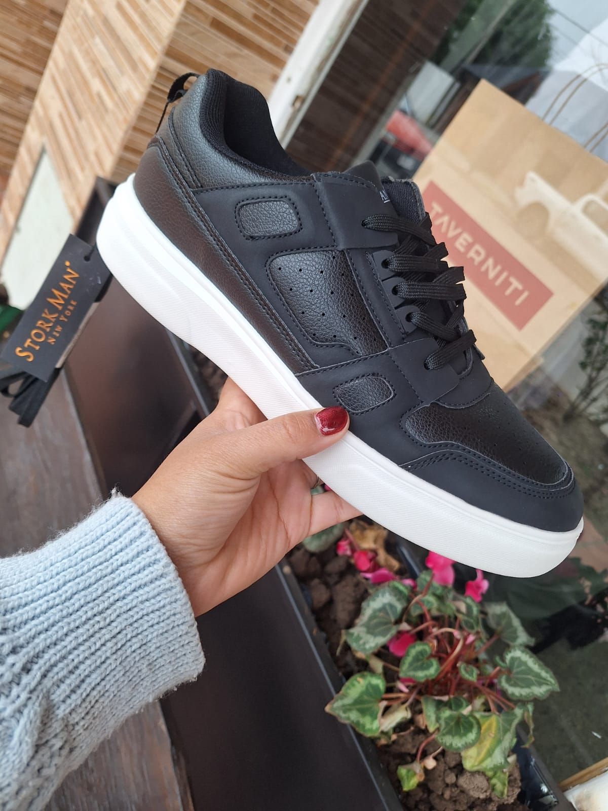 Zapatilla negra con suela blanca sostenida por una mano; fondo de escaparate.