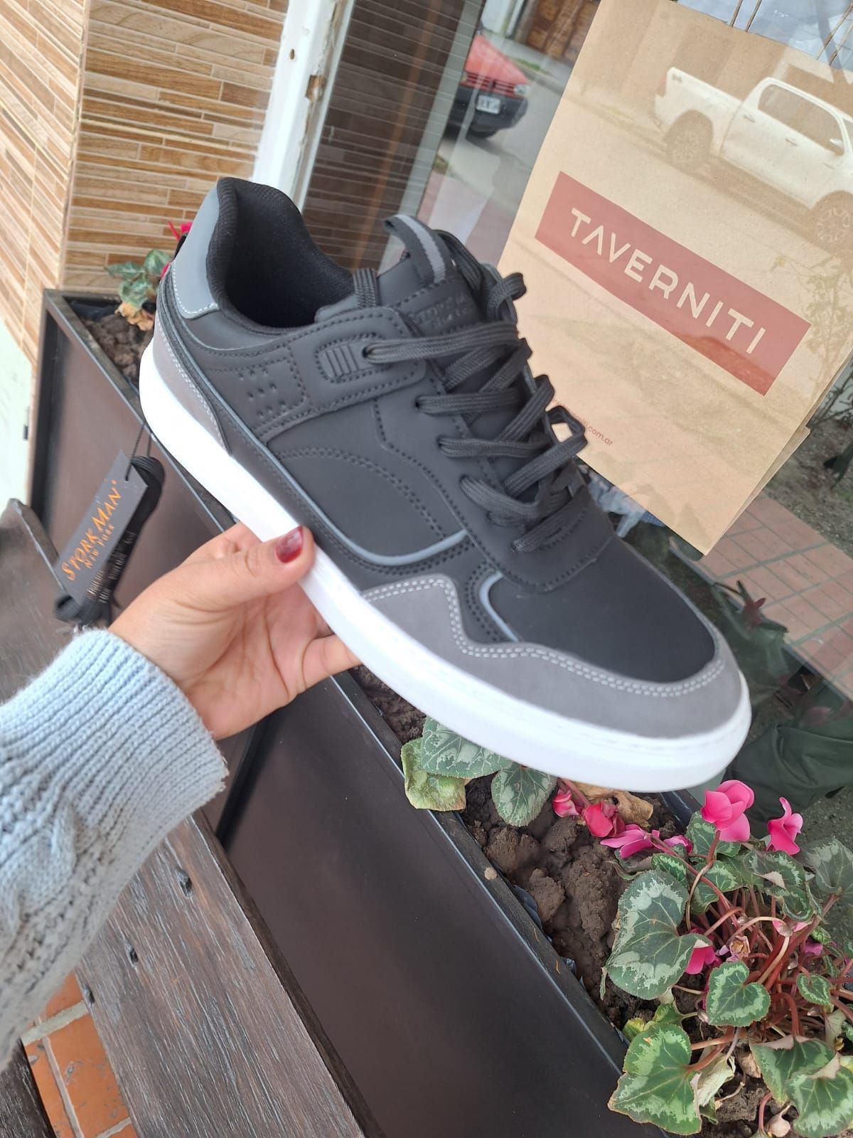 Persona sosteniendo una zapatilla deportiva negra y gris con suela blanca.