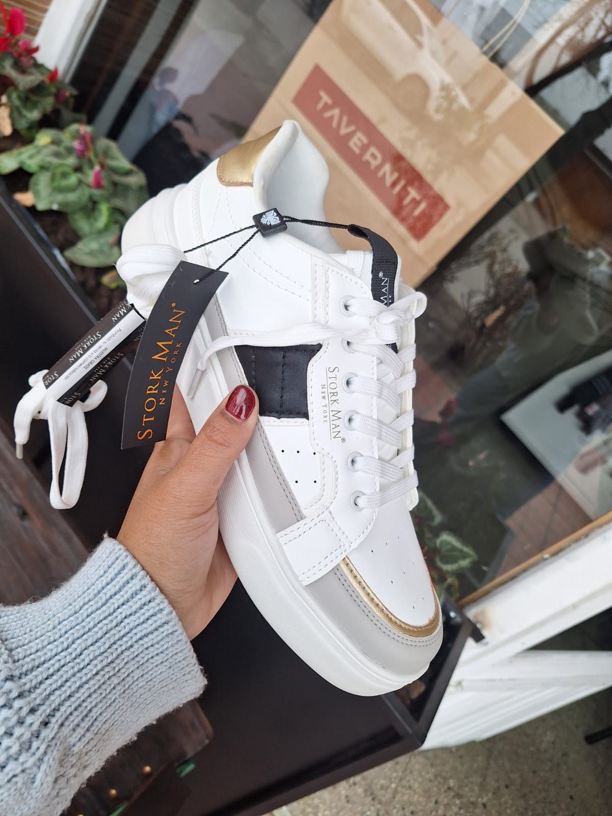 Una persona sosteniendo una zapatilla blanca y gris con un borde dorado y una raya negra.