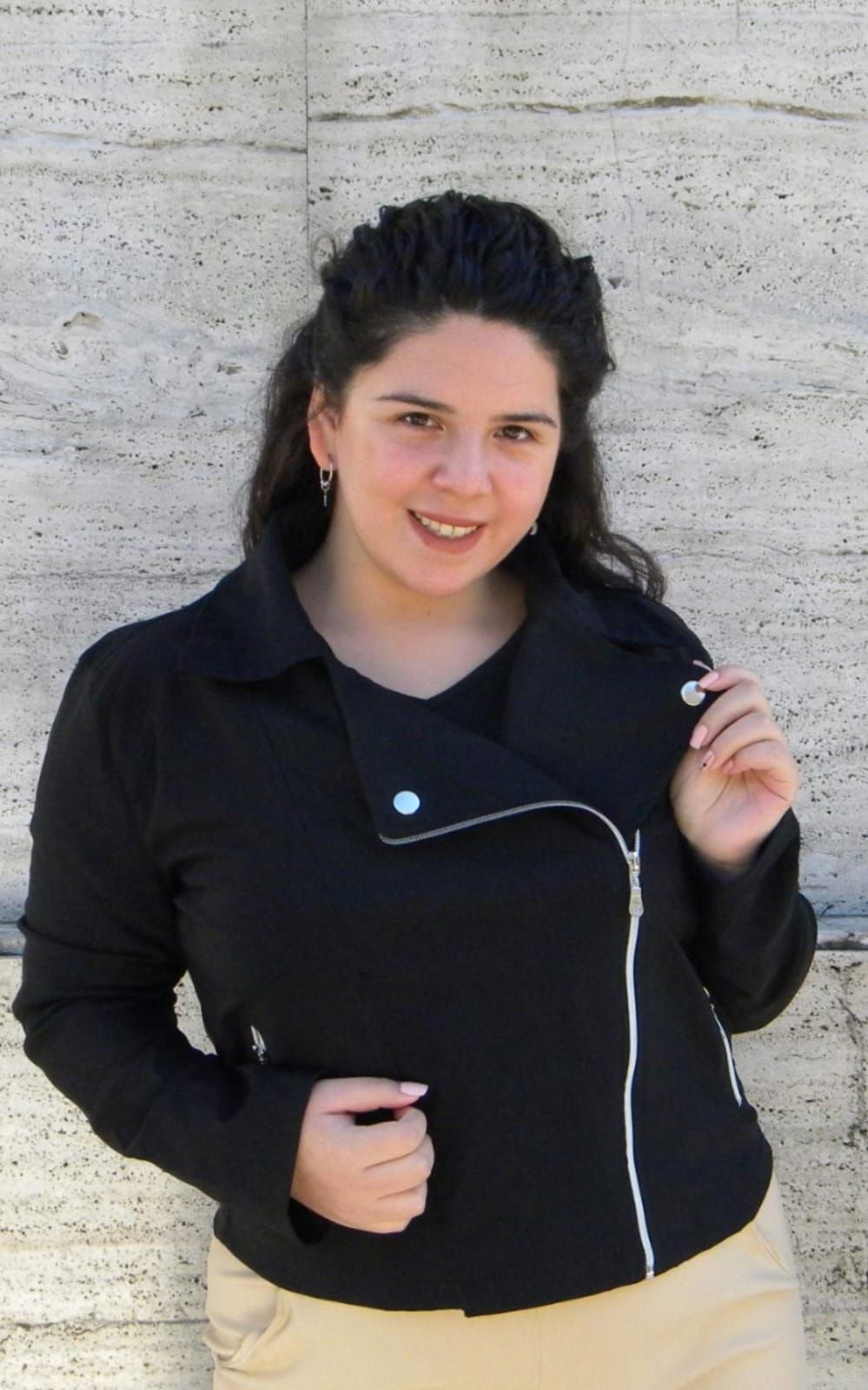 Mujer con chaqueta y falda negras, sonriendo y posando sobre un fondo blanco.