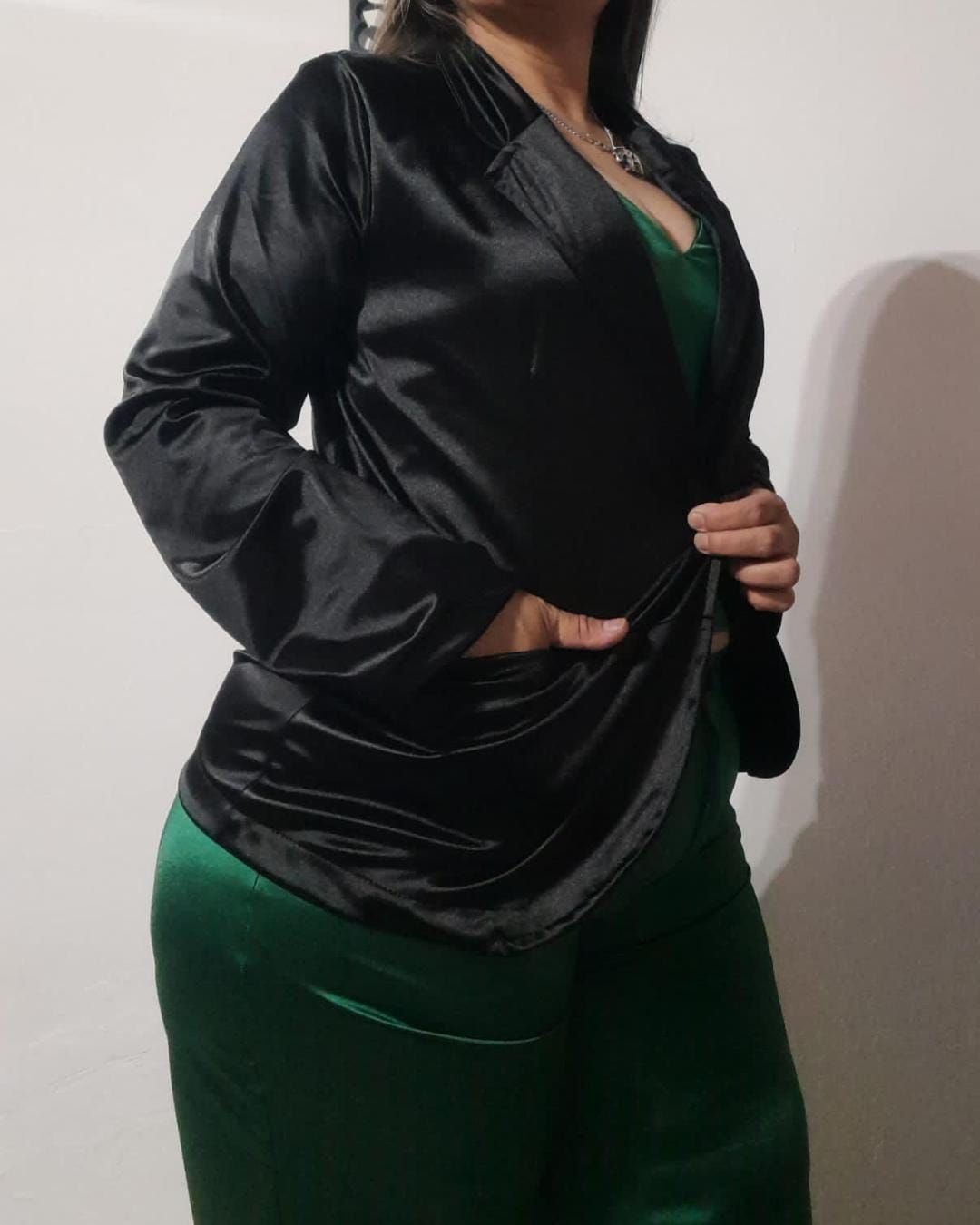 Mujer con traje de satén verde, blazer de terciopelo negro y manos en los bolsillos.