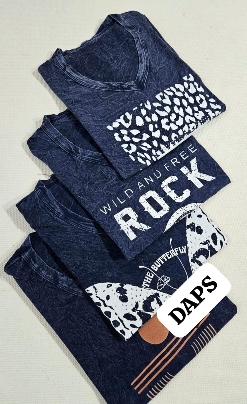 Dos camisetas azules de estrella de rock, una de ellas doblada y con texto blanco en el frente.