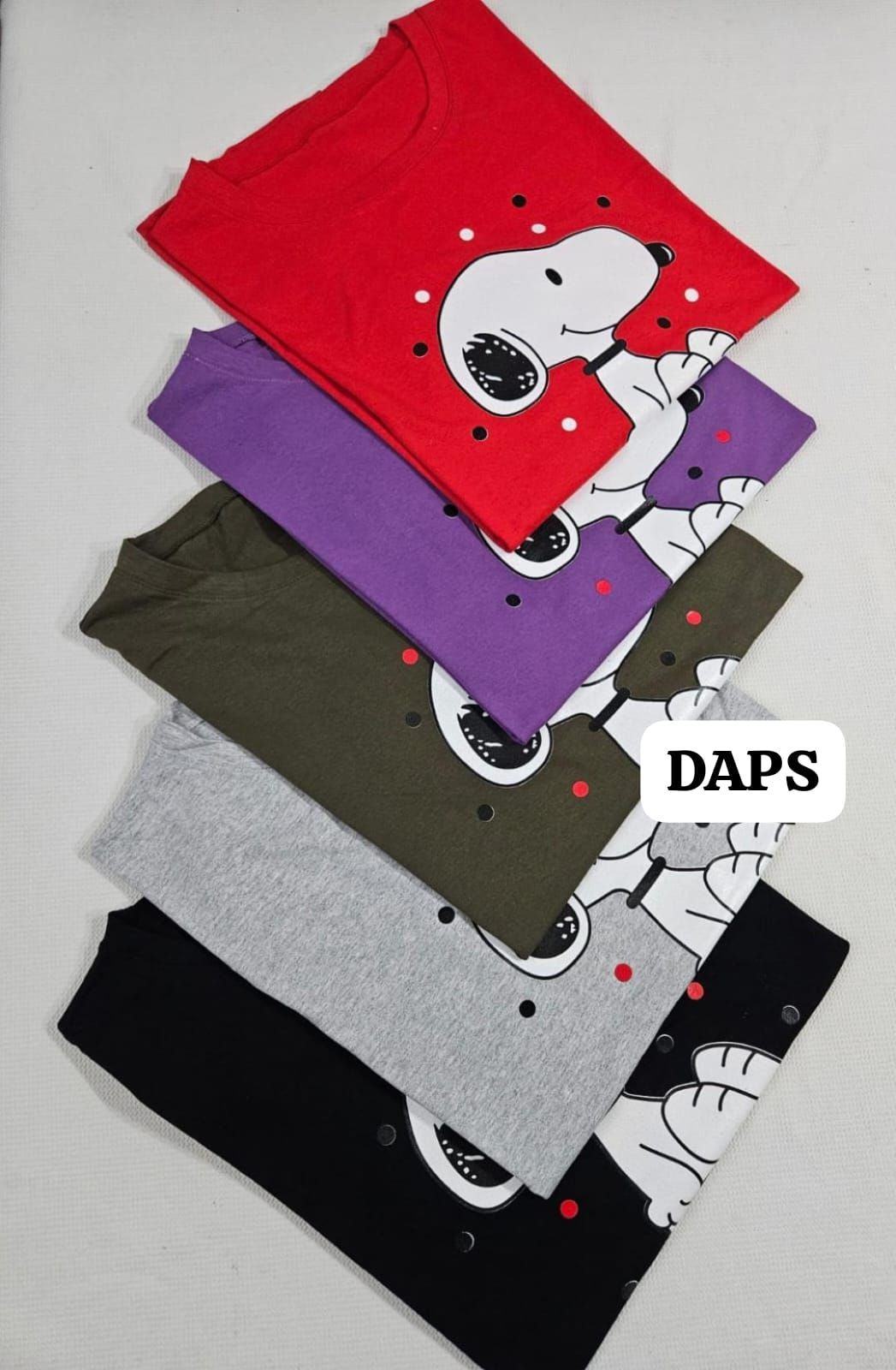 Dos camisetas de Snoopy, verde oliva y negra, con una ilustración blanca. Puntos rojos y grises rodean a Snoopy.