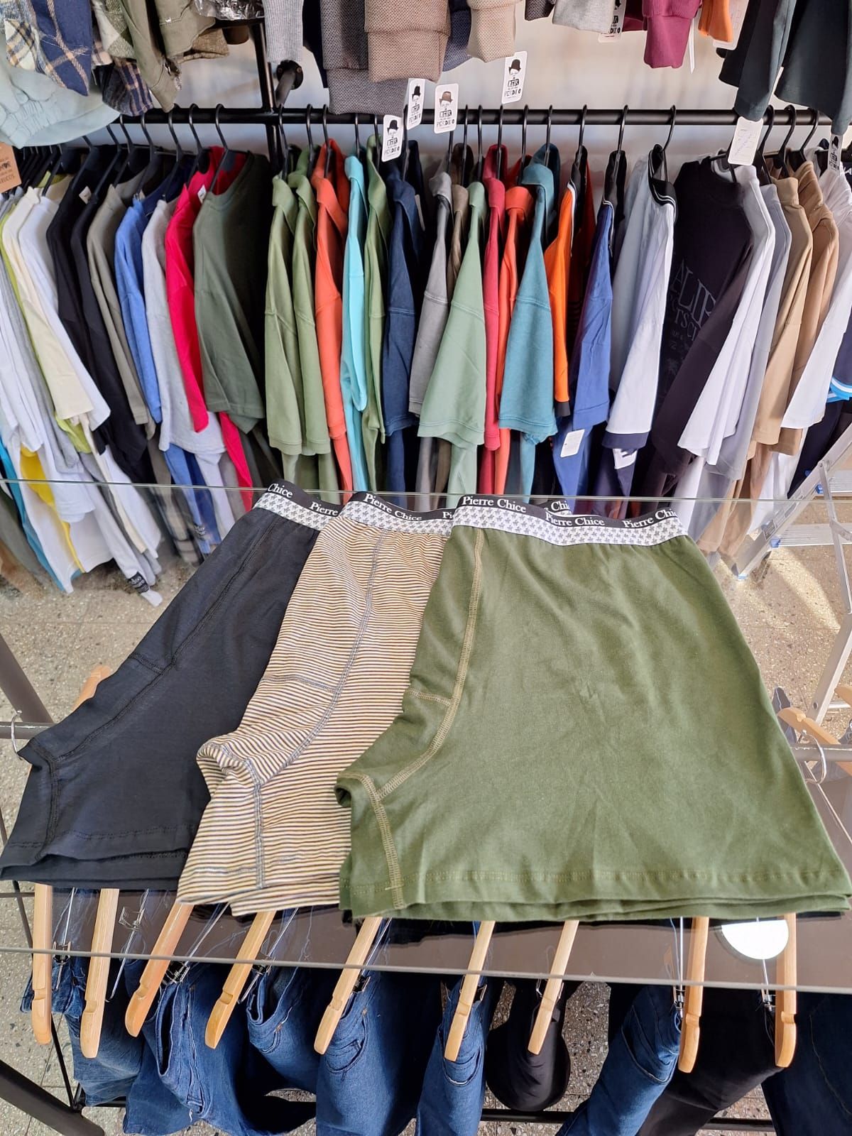 Tres pares de calzoncillos bóxer para hombre, de color negro, verde y tostado, apilados en un soporte de metal en una tienda.