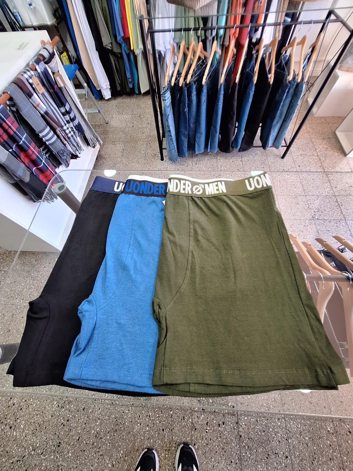 Tres pares de calzoncillos bóxer: negro, azul y verde, expuestos en un perchero de ropa en una tienda.