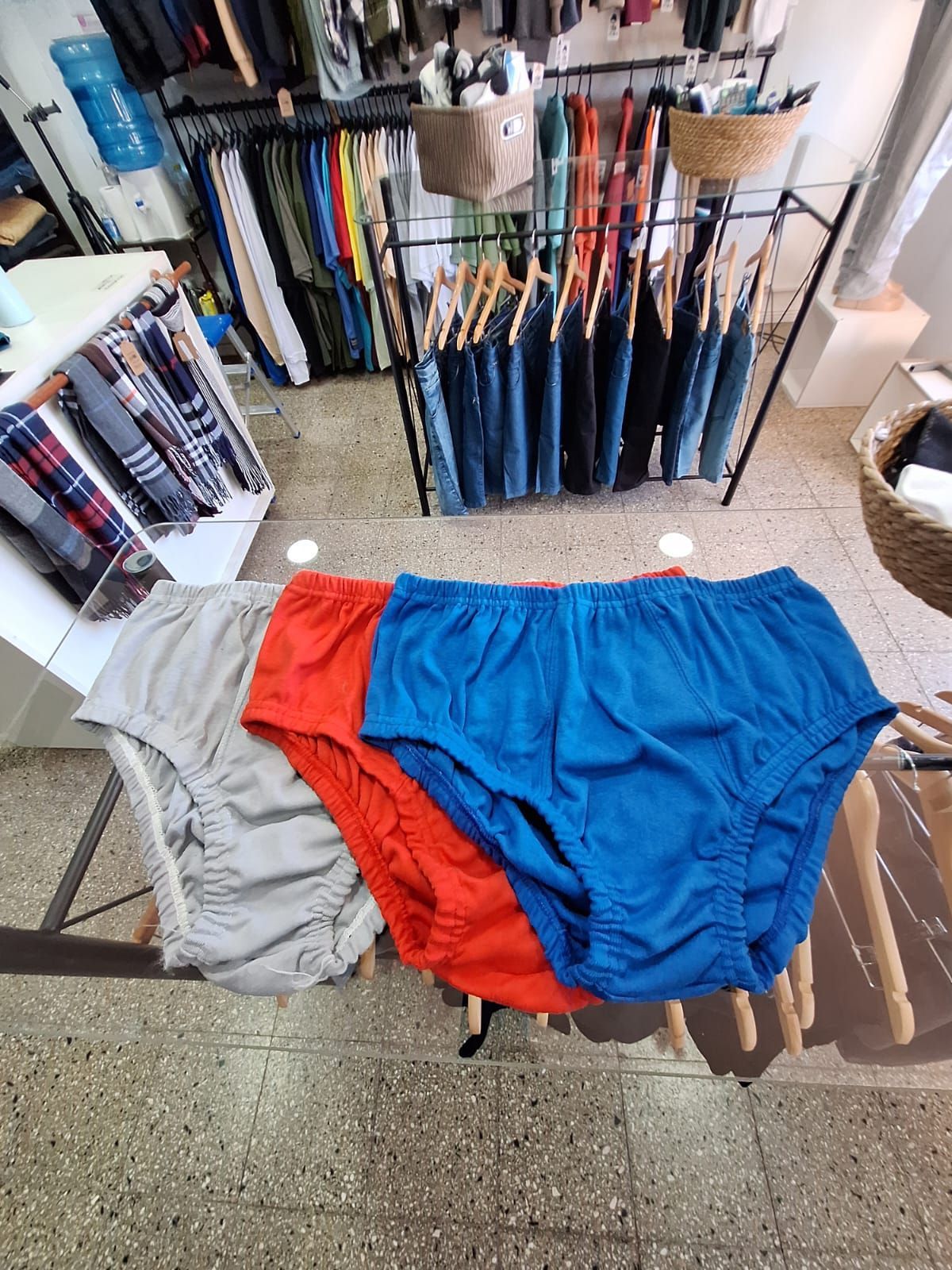 Tres pares de calzoncillos coloridos: azul, rojo y gris, dispuestos sobre una mesa de cristal en una tienda.