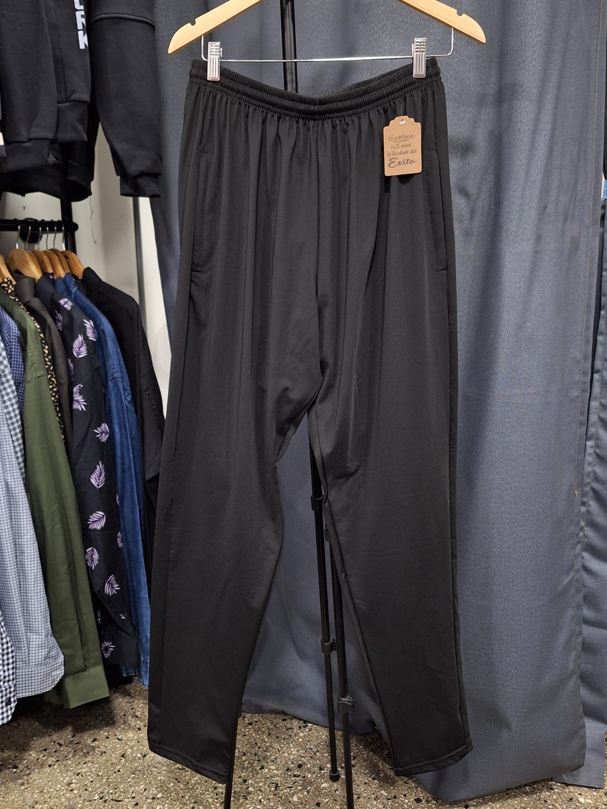 Pantalones deportivos Puma negros colgados en un perchero, con cordón blanco y logotipo.