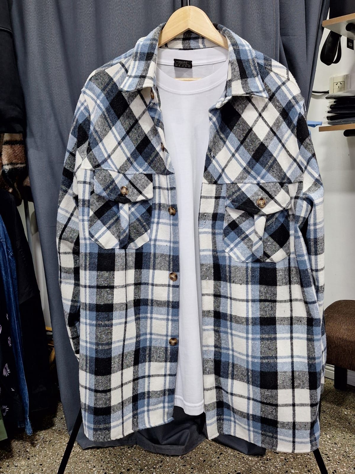 Tres camisas a cuadros en tonos tostados, azules y verdes colgadas en perchas de madera.