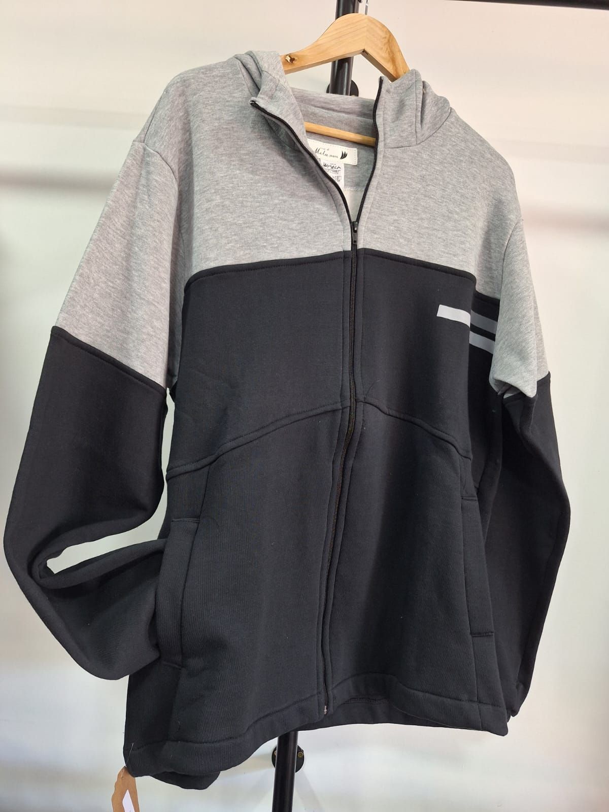 Sudadera con capucha y cremallera de color gris y azul marino colgada en un perchero.