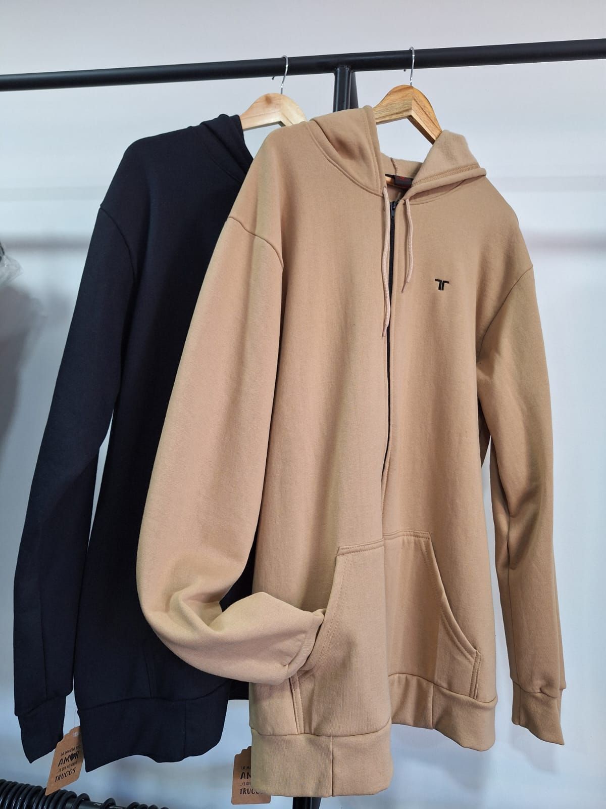 Sudadera con capucha color canela y cremallera colgada en un perchero.
