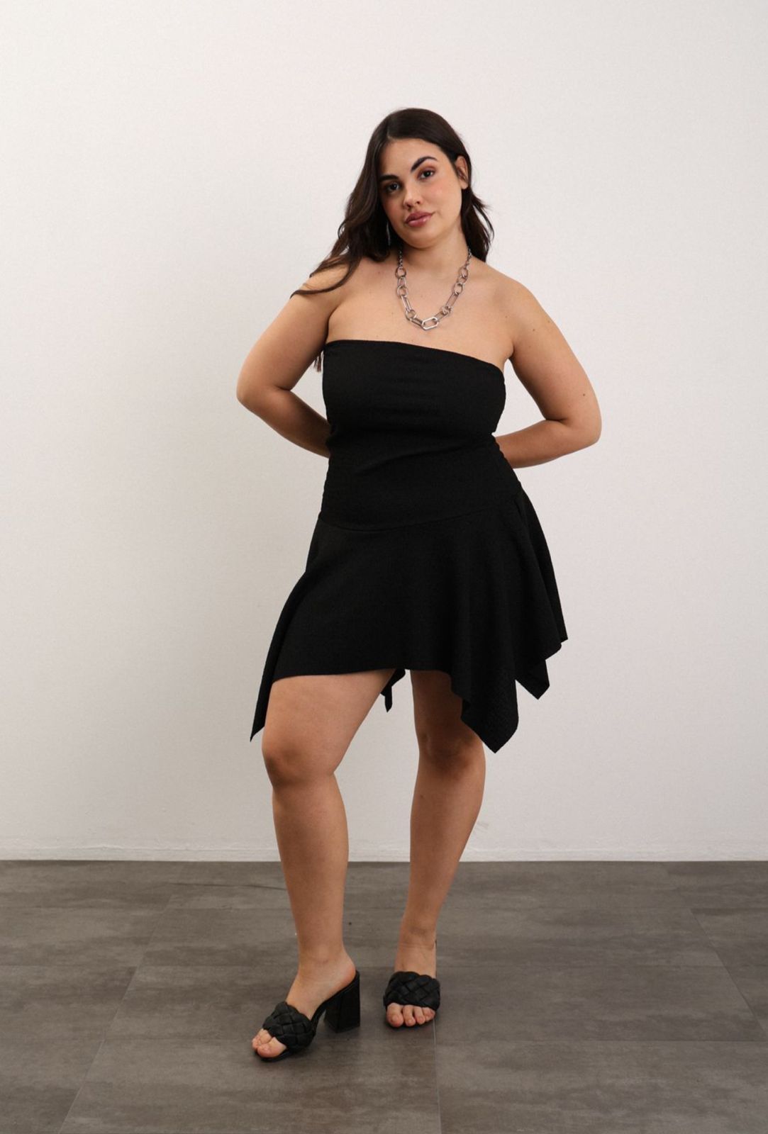 Mujer con vestido blanco sin tirantes, gafas de sol y cinturón negro, posando sobre un fondo azul.