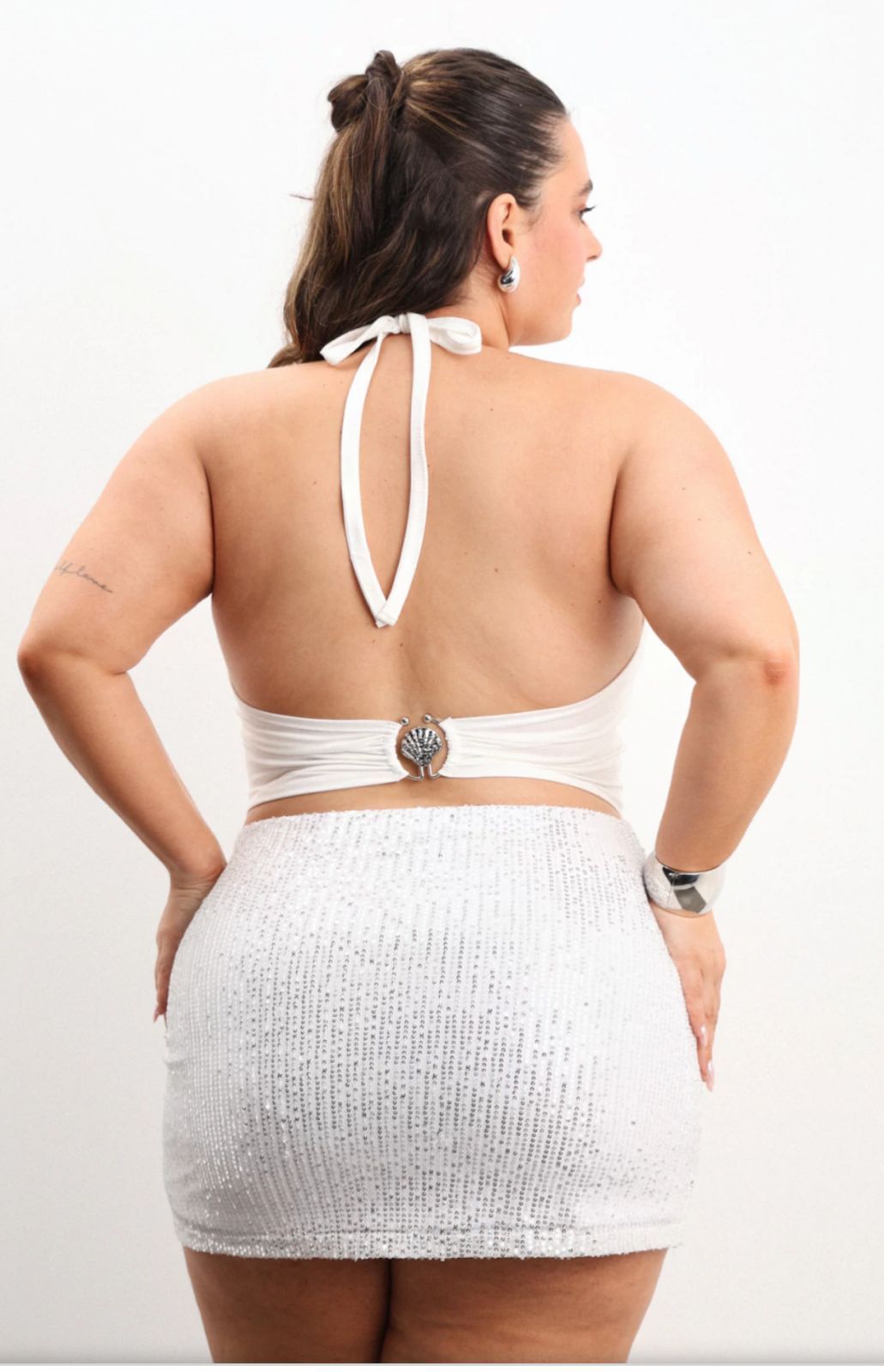 Mujer con top blanco y minifalda, posando.