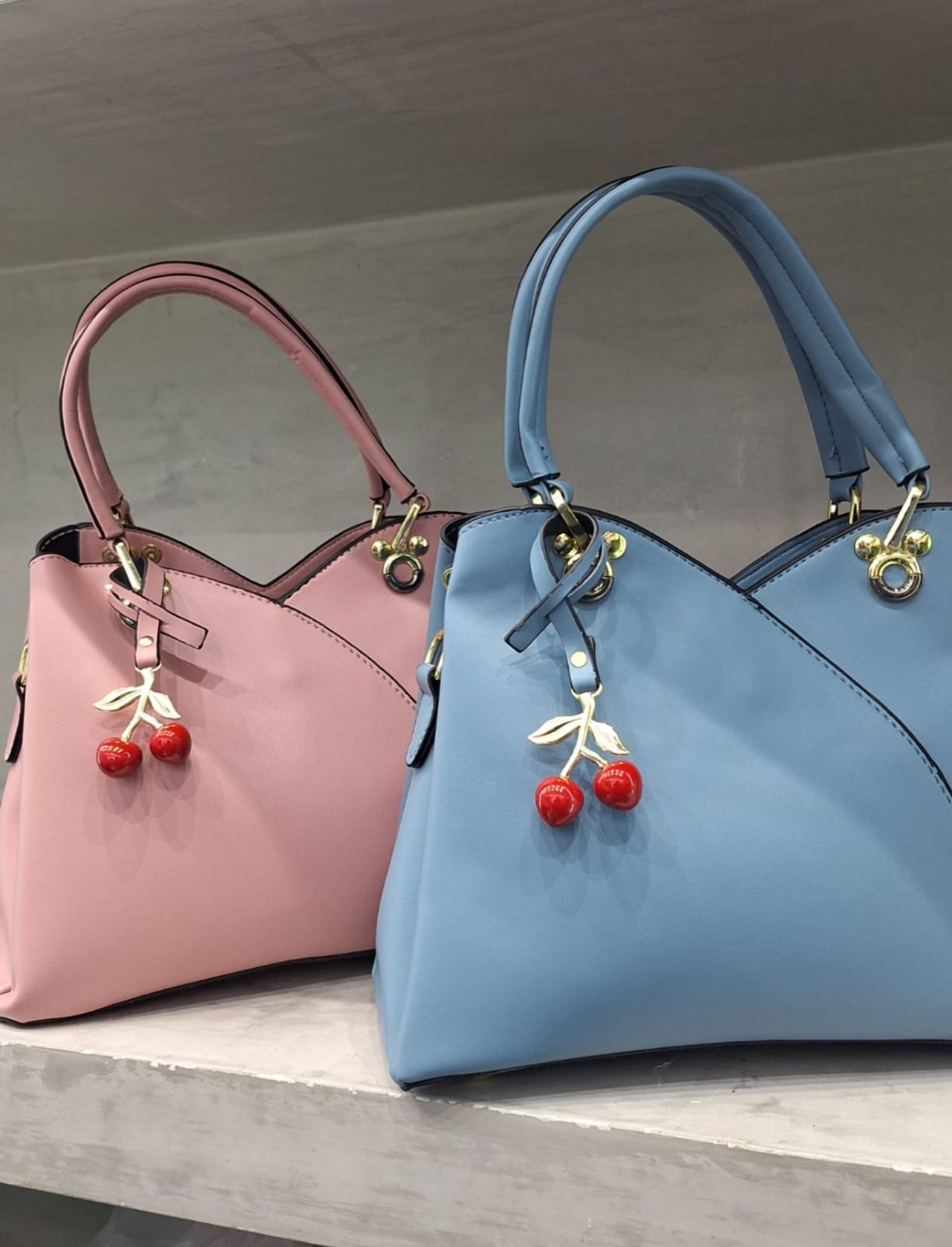 Dos bolsos de piel, uno rojo y otro negro, con charms en forma de cereza colgando de las asas.