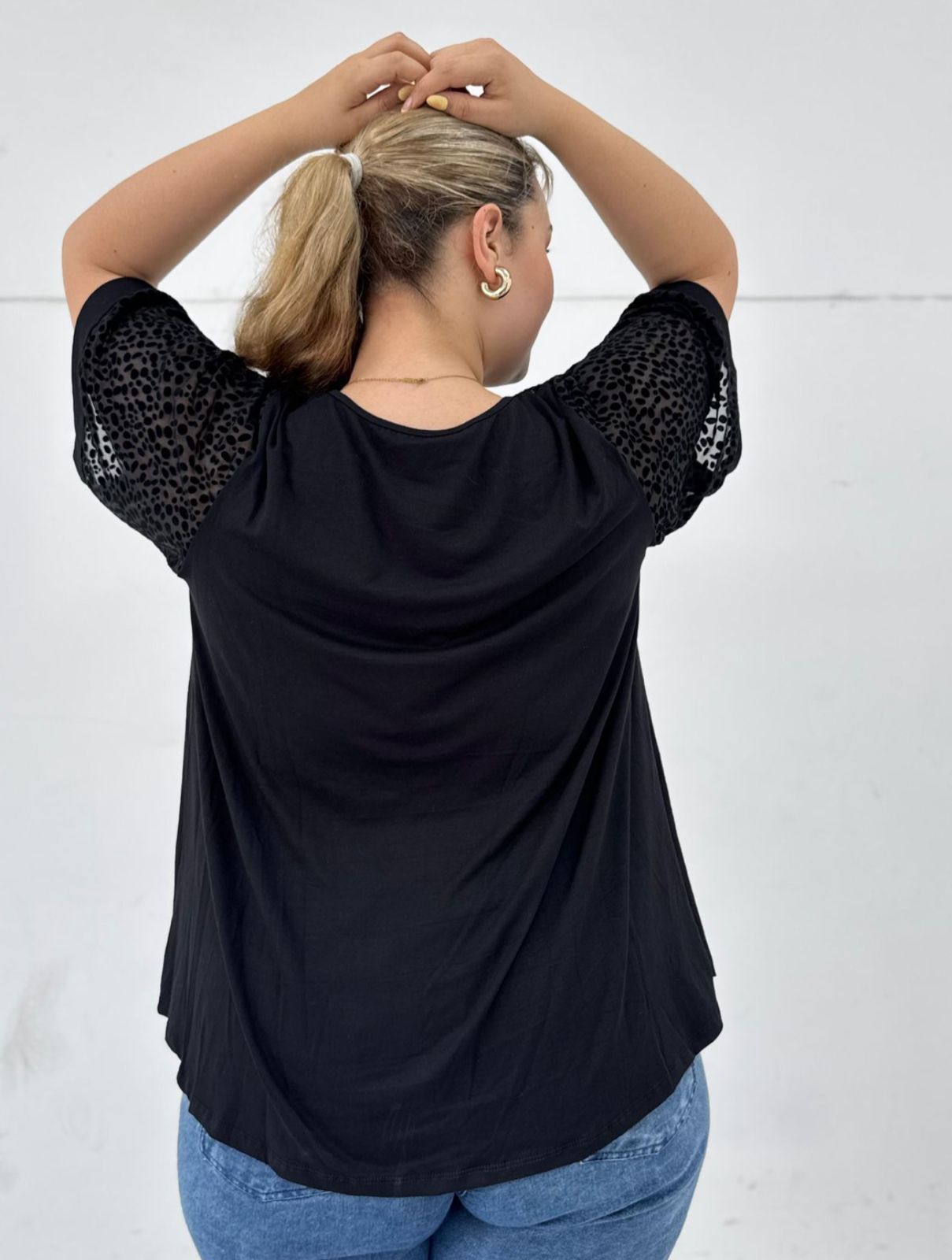 Mujer con top negro y jeans, sosteniendo un bolso blanco, sonriendo frente a una pared blanca.