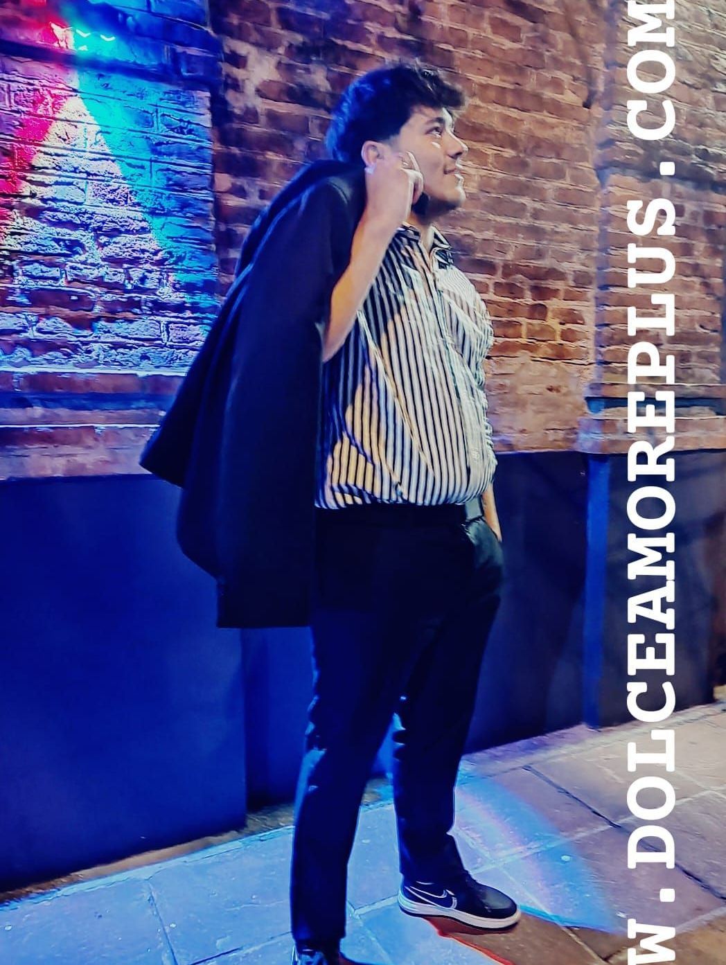 Hombre con camisa a rayas y pantalón negro sosteniendo una chaqueta