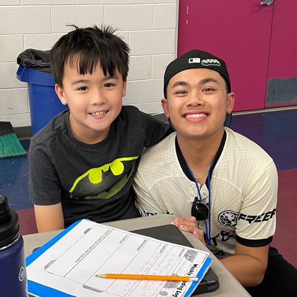 Counselor with boy child posing at a table with pink door behind them.