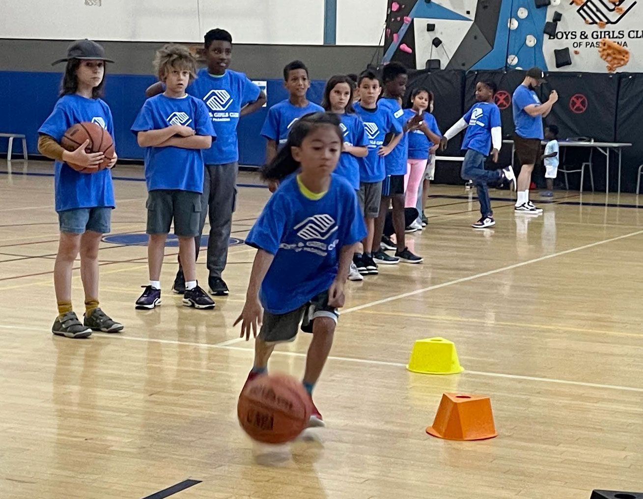group of kids watch as girls bounces basketball through a series of obstacles