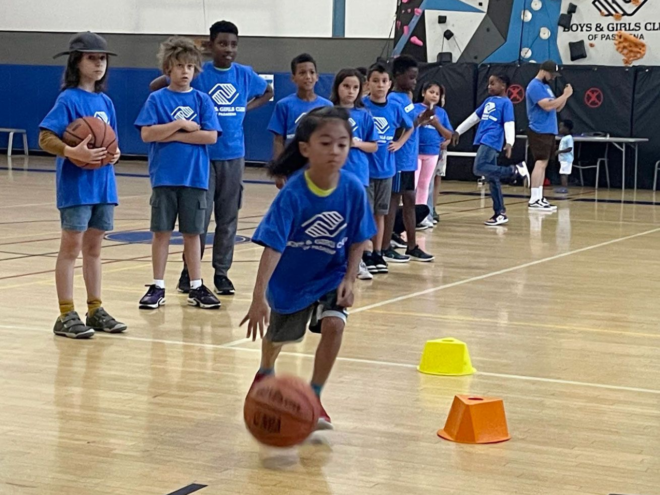 group of kids watch as girls bounces basketball through a series of obstacles