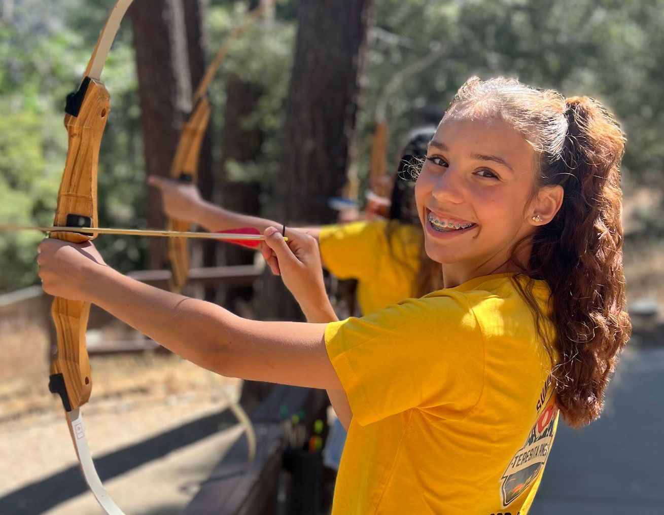 teen girl with a smile on her face is holding a bow and arrow