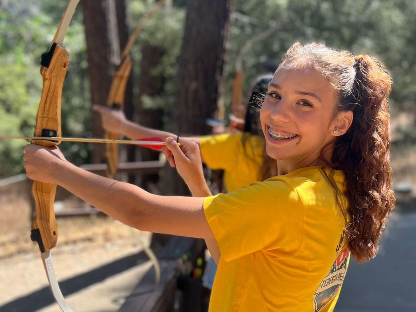 teen girl with a smile on her face is holding a bow and arrow