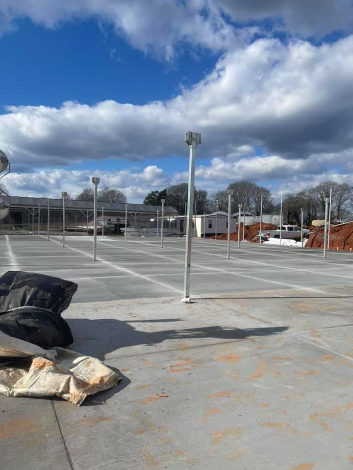 Empty gray parking lot with tall silver light poles on a cloudy day.