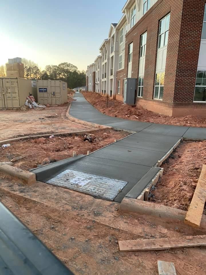 Newly poured concrete sidewalks at a construction site, alongside a brick building.